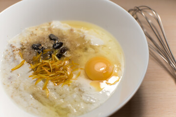 Porridge made from cake dough with orange zest and raisins is kneaded with a metal whisk in a white macro plate with a bright egg yolk