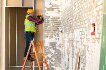 Repairman on a ladder drilling with a machine into a ceiling