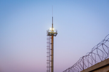 A tower with lanterns and a barbed wire fence.