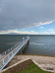 Fototapeta na wymiar Fishing pier on lake on a cloudy day. Calm waters with a background of the mountains in San Rafael, Mendoza. Dense gray clouds covering the sky.