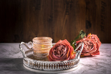 Drei Rosen in Alt Rose' Farben und ein Kerzenständer mit Perle liegen auf dem Holzhintergrund auf dem weißen Tablett aus Metall. Vintage, Querformat. Hintergrund. Stillleben, Postkarte