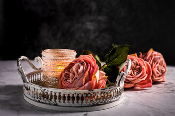 Drei Rosen in Alt Rose' Farben und ein Kerzenständer mit Perle liegen auf dem Marmorhintergrund, auf dem weißen Tablett aus Metall. Vintage, Querformat. Hintergrund. Stillleben, Postkarte