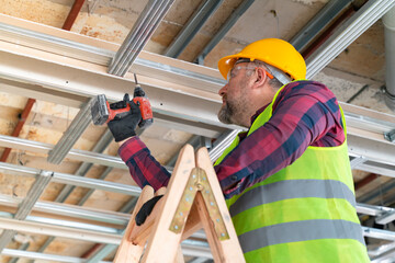 Repairman on a ladder drilling with a machine into a ceiling