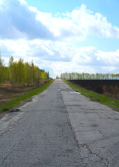 Obraz premium A broken road stretching away into the distance. To the left is a forest and to the right is a plowed agricultural field. Spring