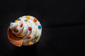 Sundae de chocolate visto desde arriba, con crema batida, rockets ,una bombilla y un trozo de cucurucho sobre un fondo negro