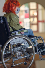 Disabled girl with red hair wearing a mask in a wheelchair, selective focus