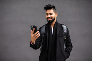 Handsome young man dressed in stylish clothes chatting on smart phone while standing on the city street.