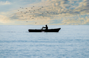 Rowing boat on the sea. Fishing by boat. Birds on the horizon. Silhouettes.
