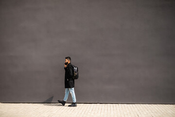 Young man talking on the phone walkin on the street on gray background wall. Lifestyle, technology.