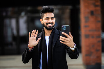 Young man holding and talking on smartphone via video call while sitting in city outdoors