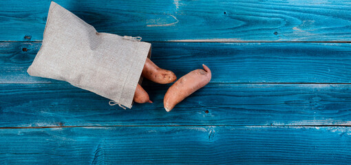 Burlap bag filled with sweet potatoes spilling out on to blue rustic wooden table