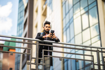 Low angle view of business man using mobile phone on city street near bridge