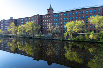 Old brick  mill buildings  (now apartments) with clock tower and their reflection in the Nashua River, New Hampshire in spring