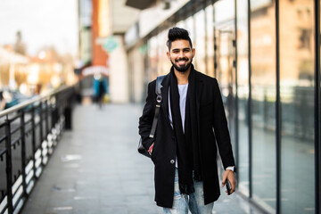 Portrait of a trendy young man with backpack walking in the city street.