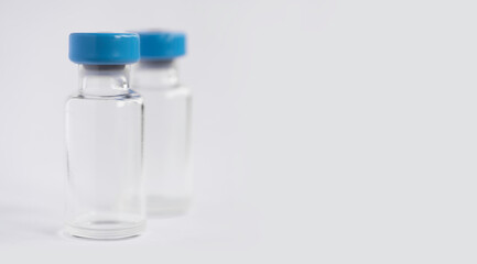 Two glass corona vaccine bottles or vials with blue cap on a on white background. Shallow depth of field. Copy space
