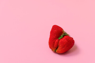 Red ripe ugly strawberry on pastel pink background with space for text. Food waste concept