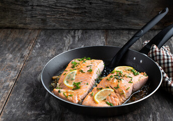 Grilled salmon fillets with lemon and herbs in roasted pan on wooden table