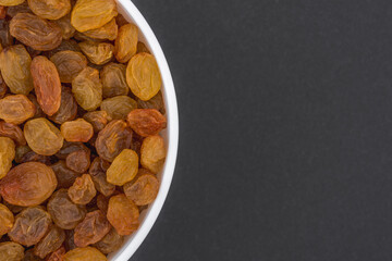 White glass bowl of yellow raisins Isolated on a dark grey background.