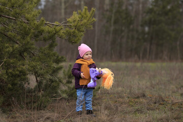 a girl in a purple jacket and an orange knitted scarf holds a toy with one hand and smiles
