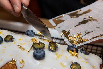 A delicious Blueberry and Lemon Loaf Cake topped with white icing, blueberries and gold leaf with a...