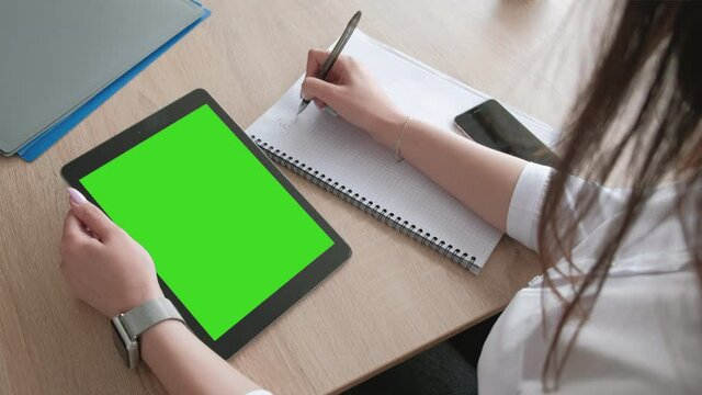 Girl makes notes in a notebook, a tablet with a chroma key
