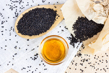 Black sesame seeds in a wooden spoon and oil on light background in the kitchen.