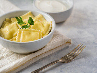 Ravioli. Nice presentation. Decorated with a sprig of mint. White background. White earthenware dishes. Next - sour cream sauce, fork. White tablecloth and white napkin.