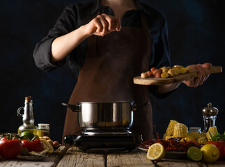 The chef prepares seafood with vegetables. The photo shows the cooking process. On a plate, seafood, on the table, vegetables, citrus fruits, a saucepan. Close-up. Dark tones.