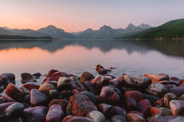Close up of the giant colorful pebbles of Lake McDonald with the towering Rocky Mountain peaks, lake reflections and a colorful pink, orange sunset at Glacier National Park, Montana, USA.