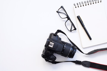 top view of work space photographer with digital camera, lens, blank notebook, pencil, glasses, camera accessory on white table background