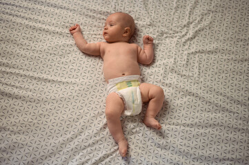 Adorable baby wearing only diaper relaxing on the bed at home