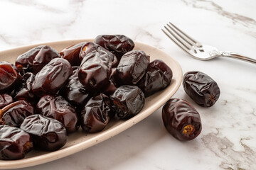 Tasty dried dates on an oval ceramic plate and fork over marble surface. Ready to eat natural...