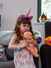 A Cute Baby Girl Sitting On A Sofa With A Doll