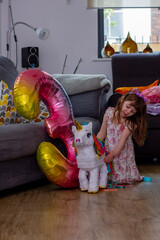 A Cute Baby Girl Sitting On The Floor With a Balloon And An Unicorn Pinata