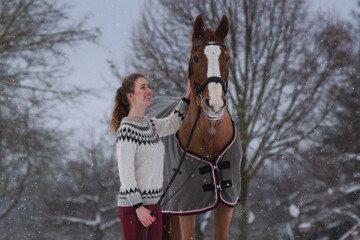 Reiterin steht neben ihrem Pferd im Winter