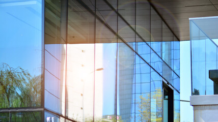 Modern glass building and rising sun. Glass facade on a bright sunny day with sunbeams in the blue sky. Economy, finances, business activity concept.  