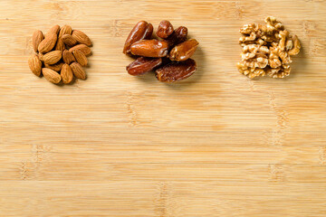 Raw almonds, organic pitted dates and walnut halves on the wooden cutting board background