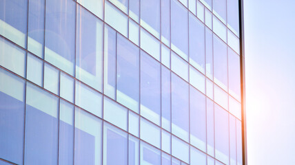 Modern glass building and rising sun. Glass facade on a bright sunny day with sunbeams in the blue sky. Economy, finances, business activity concept.  