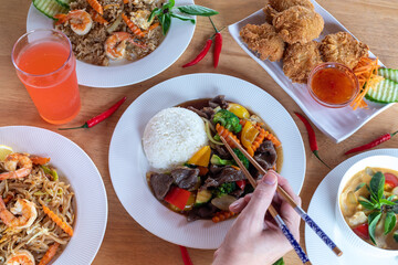 A top-down view of several varieties of  Thai food with pares chopsticks in hand with wood background. Bamboo shoots, Glass noodles, Carrot, Oyster sauce, Rice, shrimp, Cabbage, onions, strong basil, 