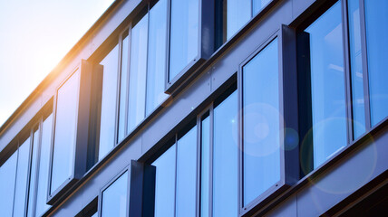 Obraz premium Modern glass building and rising sun. Glass facade on a bright sunny day with sunbeams in the blue sky. Economy, finances, business activity concept. 