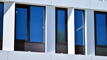 Fragment of a modern white office building. Facade of modern building. Reflection of sky in windows. Abstract blue architectural background.
