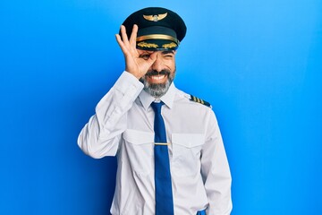 Middle age man with beard and grey hair wearing airplane pilot uniform doing ok gesture with hand...