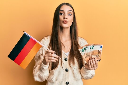 Beautiful brunette young woman holding germany flag and euros banknotes looking at the camera blowing a kiss being lovely and sexy. love expression.