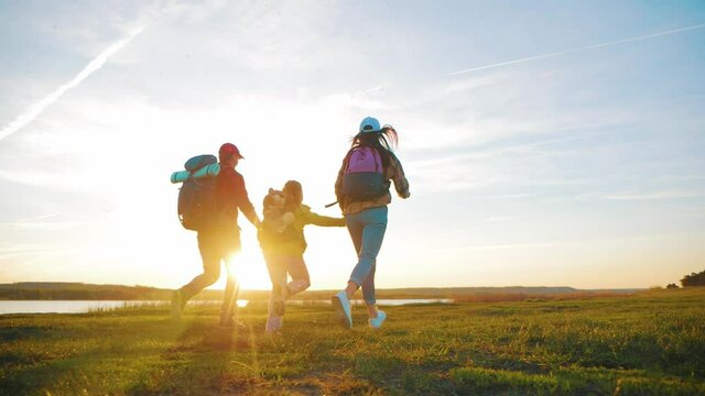 Happy family are running on hike trip. Teamwork family hiking in nature. Parents with child hiking adventure. Group of people run the field at sunset. Friendly family summer vacation together.