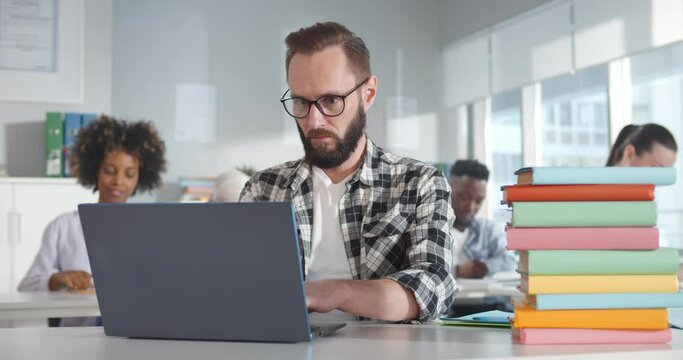 Young bearded sitting at desk and using laptop in classroom