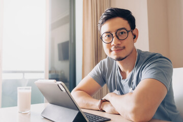 Happy Asian man is working on his tablet in concept of work from home.