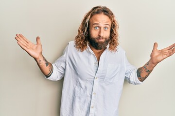 Handsome man with beard and long hair wearing casual white shirt clueless and confused with open...