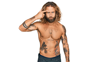 Fototapeta premium Handsome man with beard and long hair standing shirtless showing tattoos pointing unhappy to pimple on forehead, ugly infection of blackhead. acne and skin problem