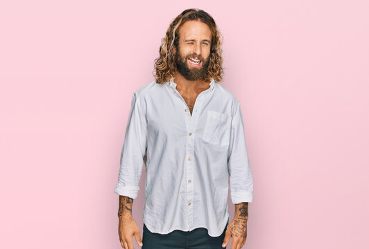 Handsome man with beard and long hair wearing casual clothes winking looking at the camera with sexy expression, cheerful and happy face.