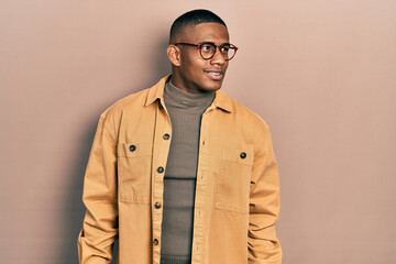 Young black man wearing casual clothes and glasses looking away to side with smile on face, natural expression. laughing confident.